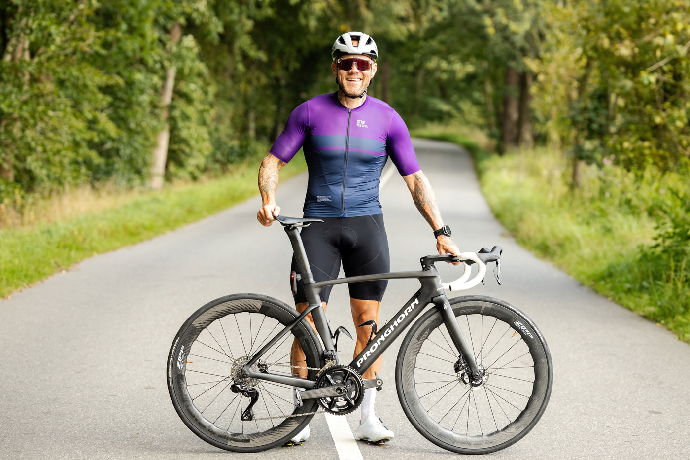 Anders står på en landevej og holder sin cykel som om han lige er stået af.